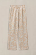 A pair of wide-leg trousers with a beige and white abstract floral pattern, displayed flat against a neutral beige background.